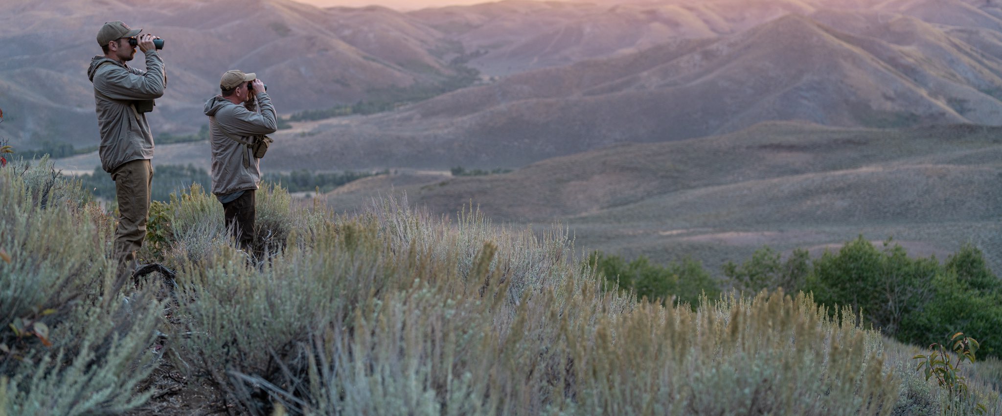 father and son with binoculars observing a scenic landscape with mountains and valleys.