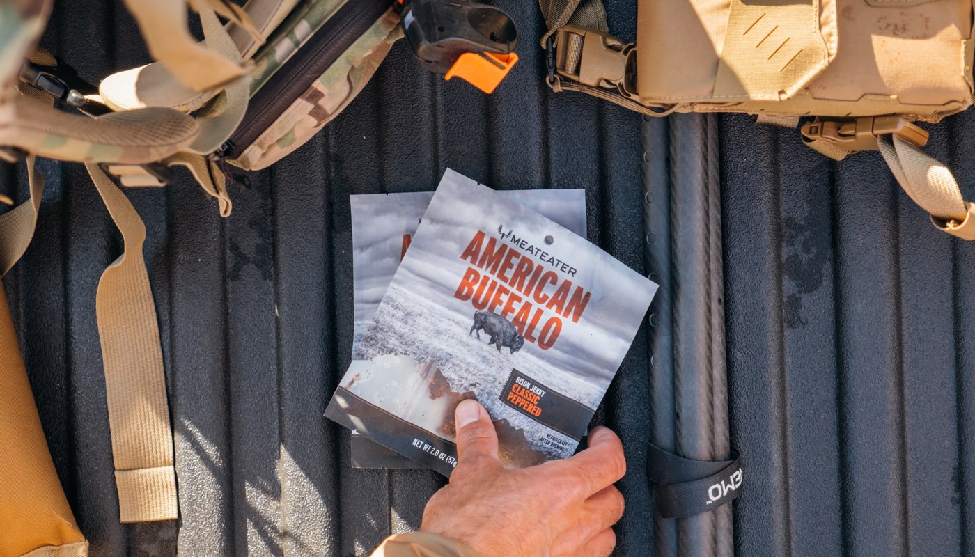 Person holding 'American Buffalo' jerky with tactical gear in the background
