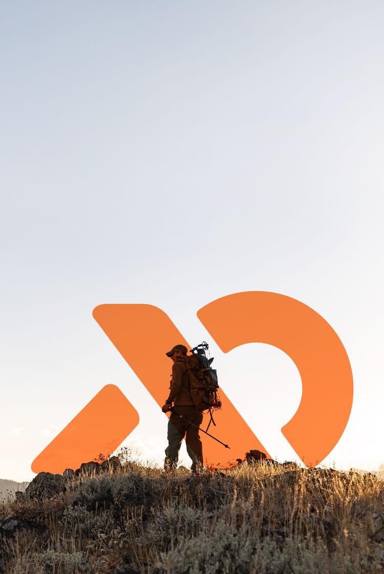 Person in hunting gear standing on a hill with an orange First Lite logo in the background