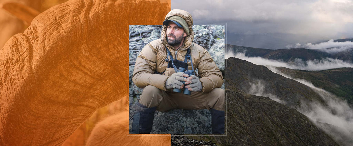 Guy with binoculars sitting in a boulder field and dressed in heavy insulated outerwear.