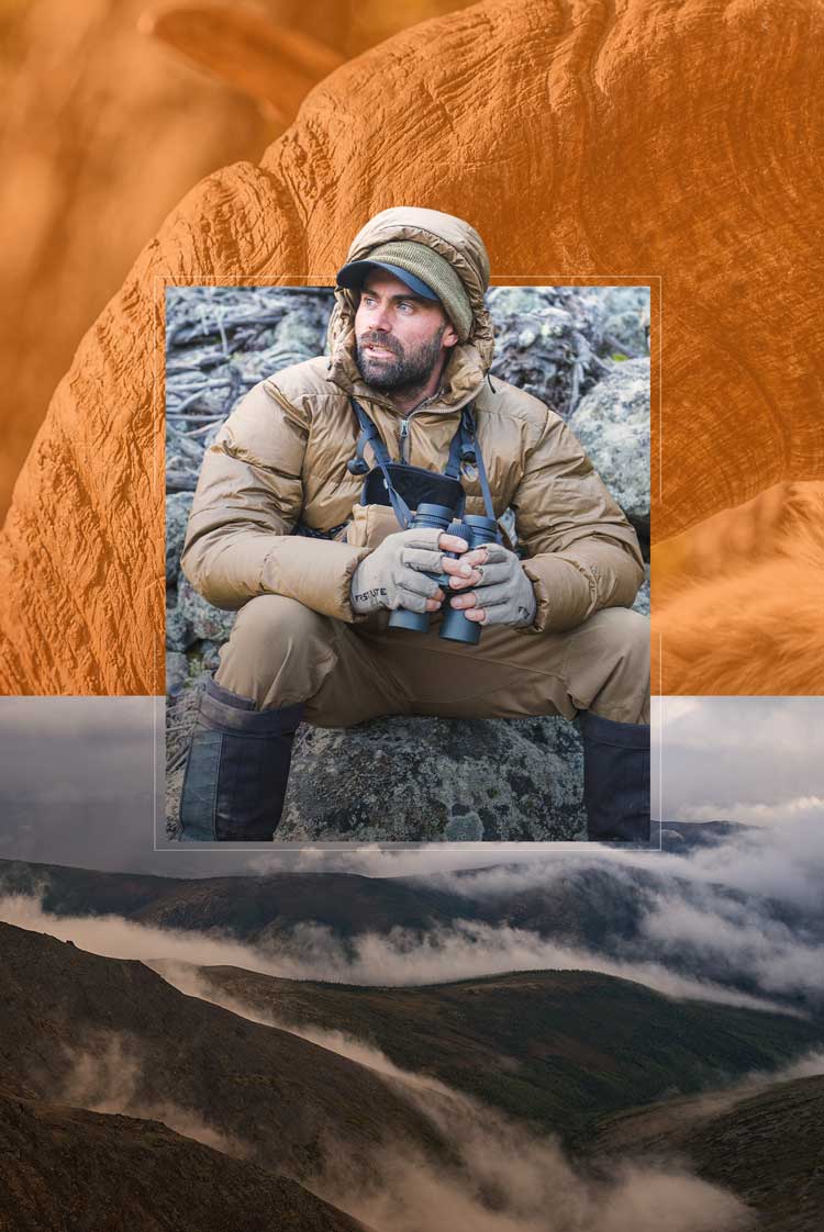 Guy with binoculars sitting in a boulder field and dressed in heavy insulated outerwear.