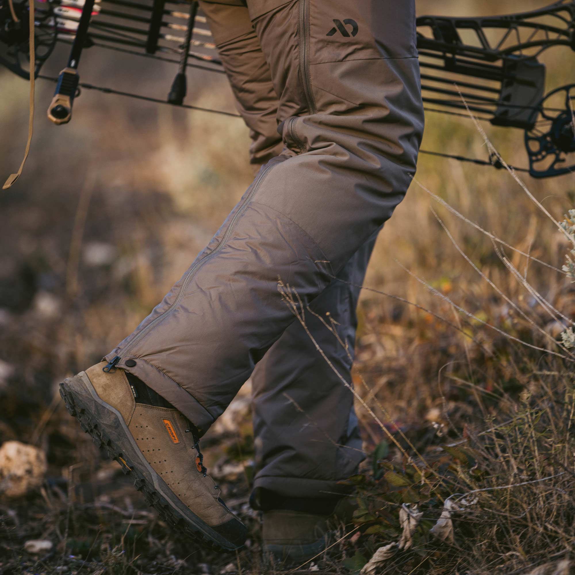 Close up of a tan puffy pant being worn by an archery hunter walking uphill.