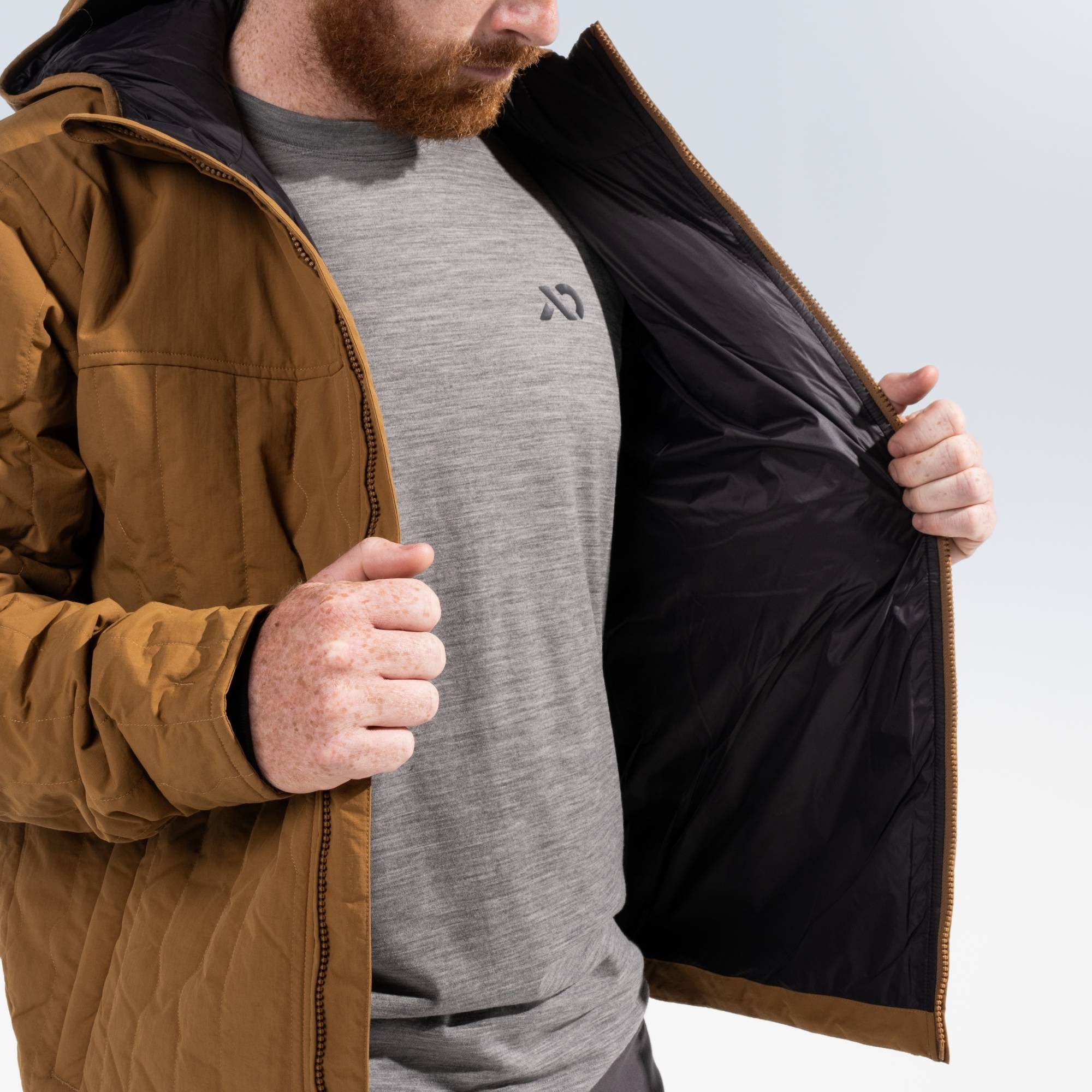 Man wearing a gray shirt with FIRST LITE logo showing the black inside of a rust outpost jacket.