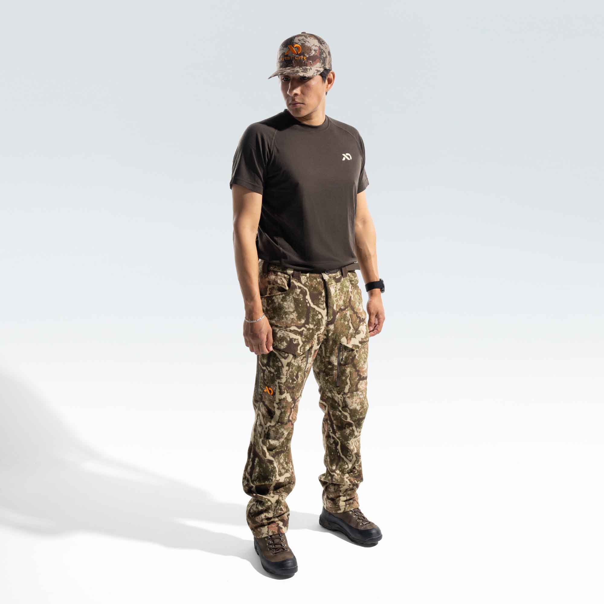 Man wearing a FIRST LITE brown shirt, camo cap and camo pants.