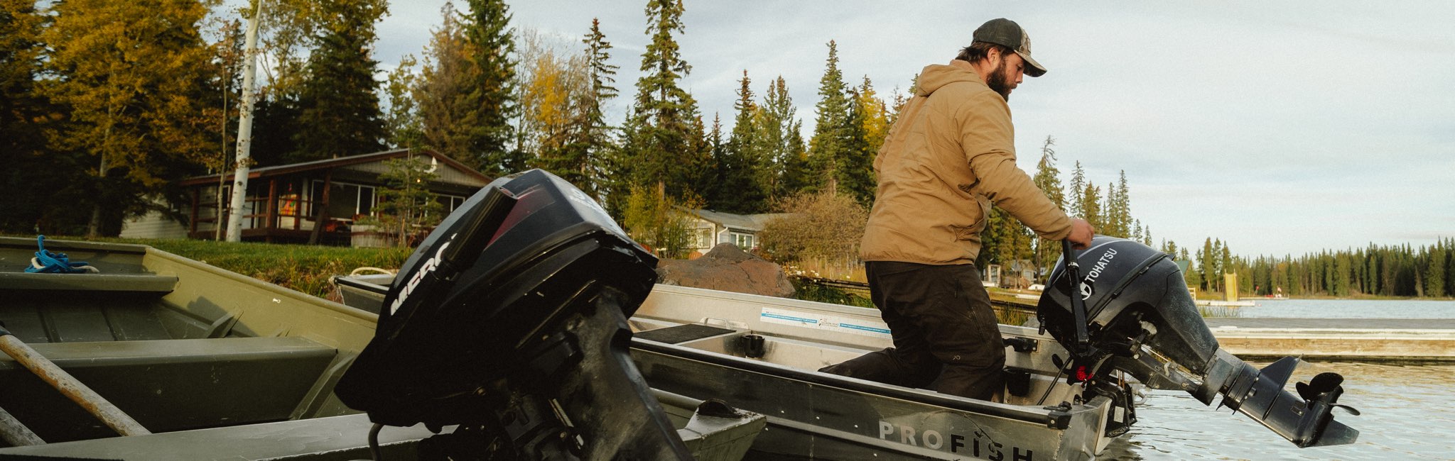 Man operating a boat with a motor on a lake surrounded by trees