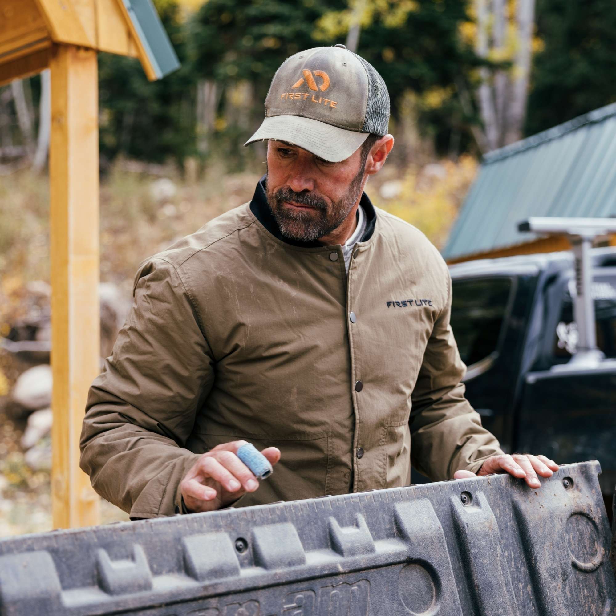 Man wearing an akern chore coat and a FIRST LITE hat closing the back of his pick up.