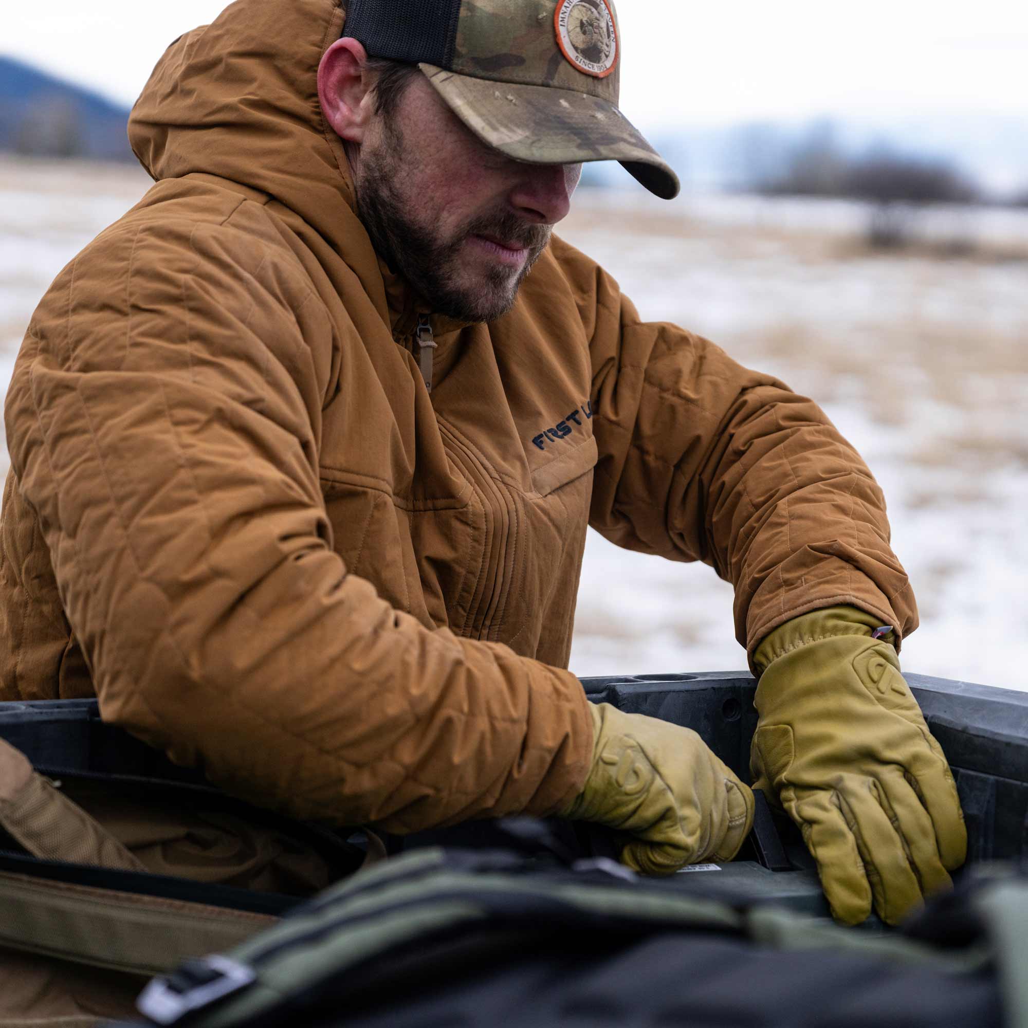 Man wearing a rust outpost jacket and a camo cap packing up stuff in his van.