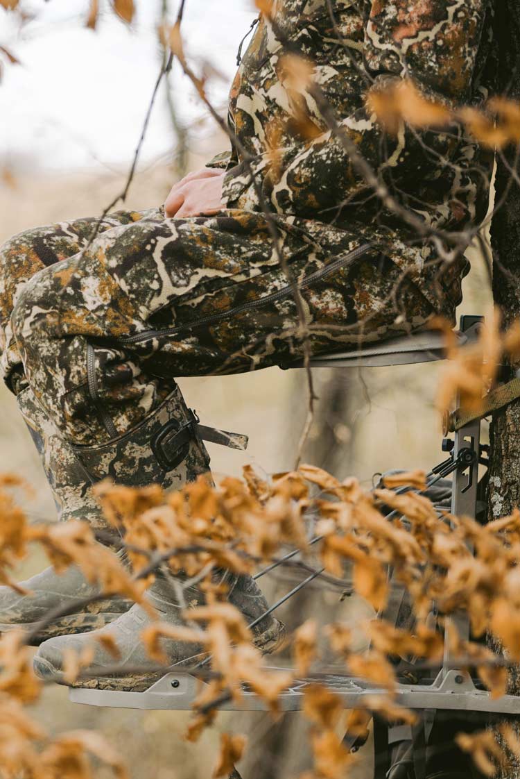 Close up of a hunter sitting in a tree stand wearing whitetail camo, boots, and insulated outerwear.