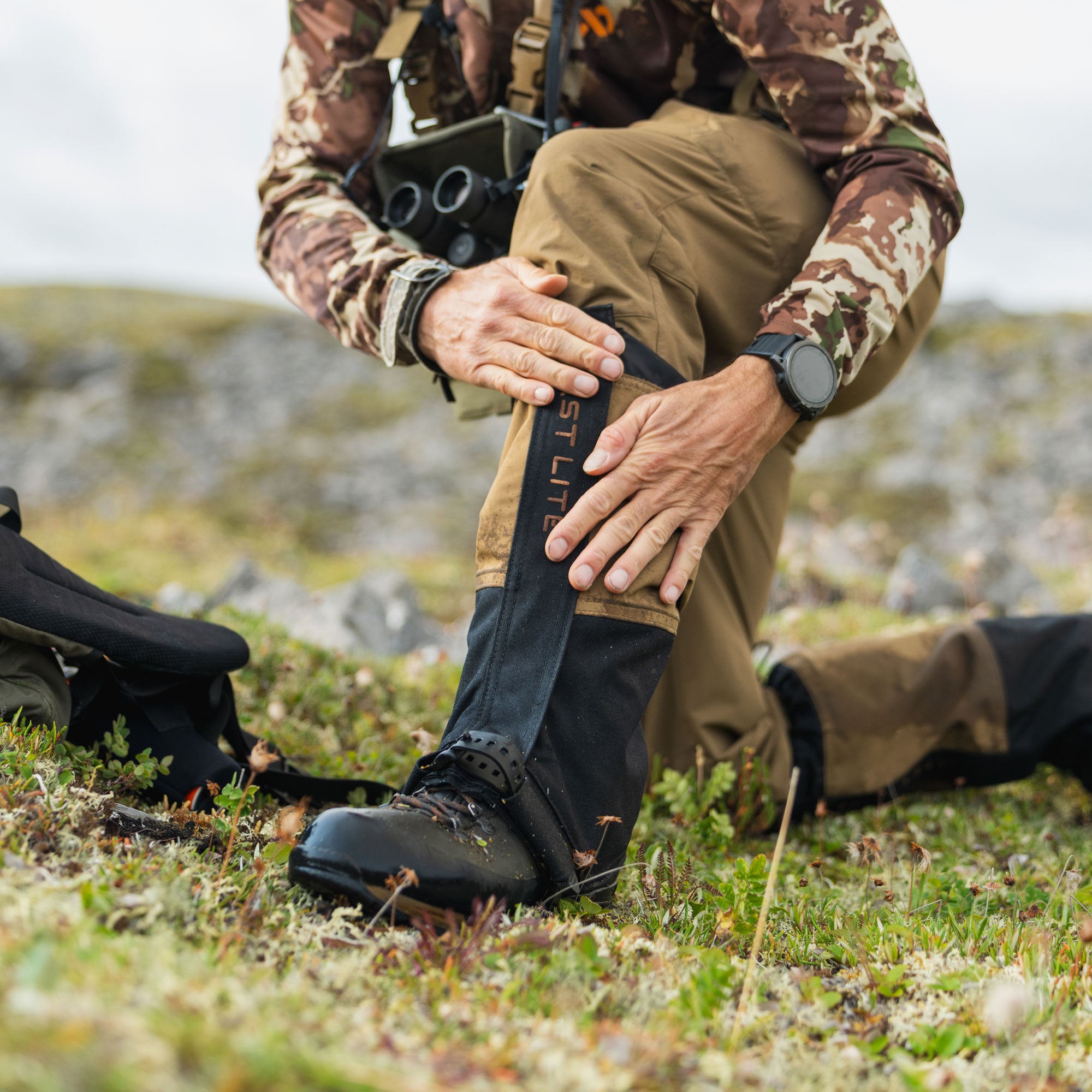 Man in the field adjusting boot gaiters in damp grass