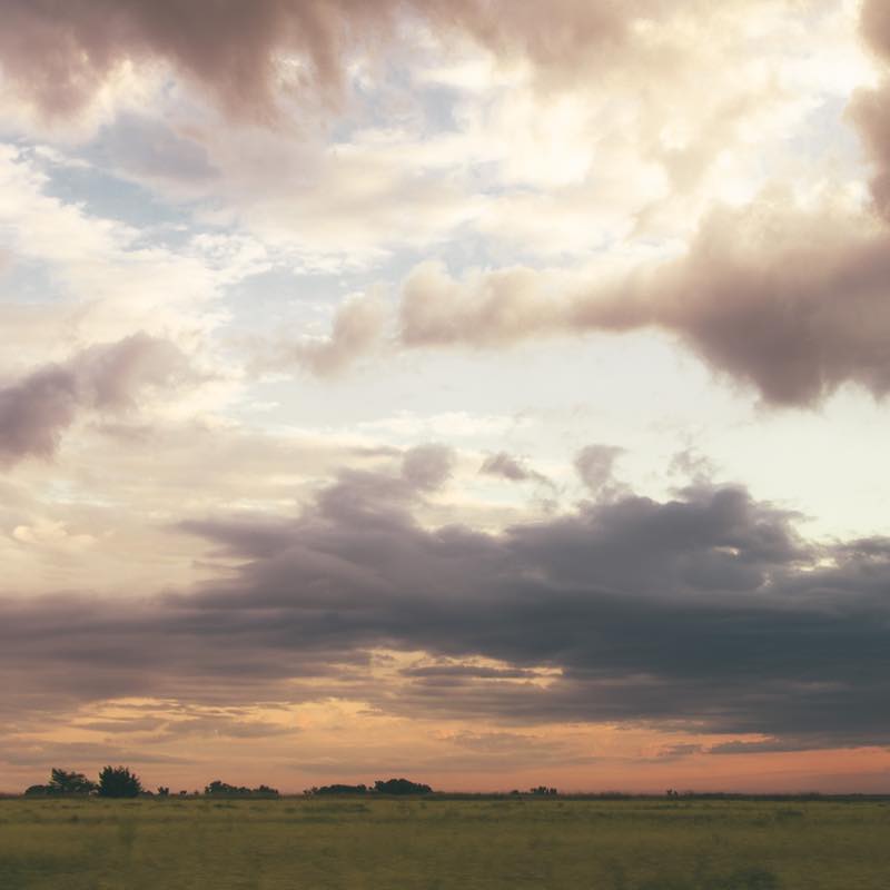 Scenic landscape with a green field under a dramatic sunset sky of orange and gray clouds.