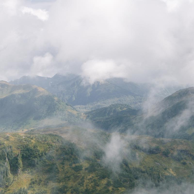 Green mountain landscape covered in white clouds and fog.
