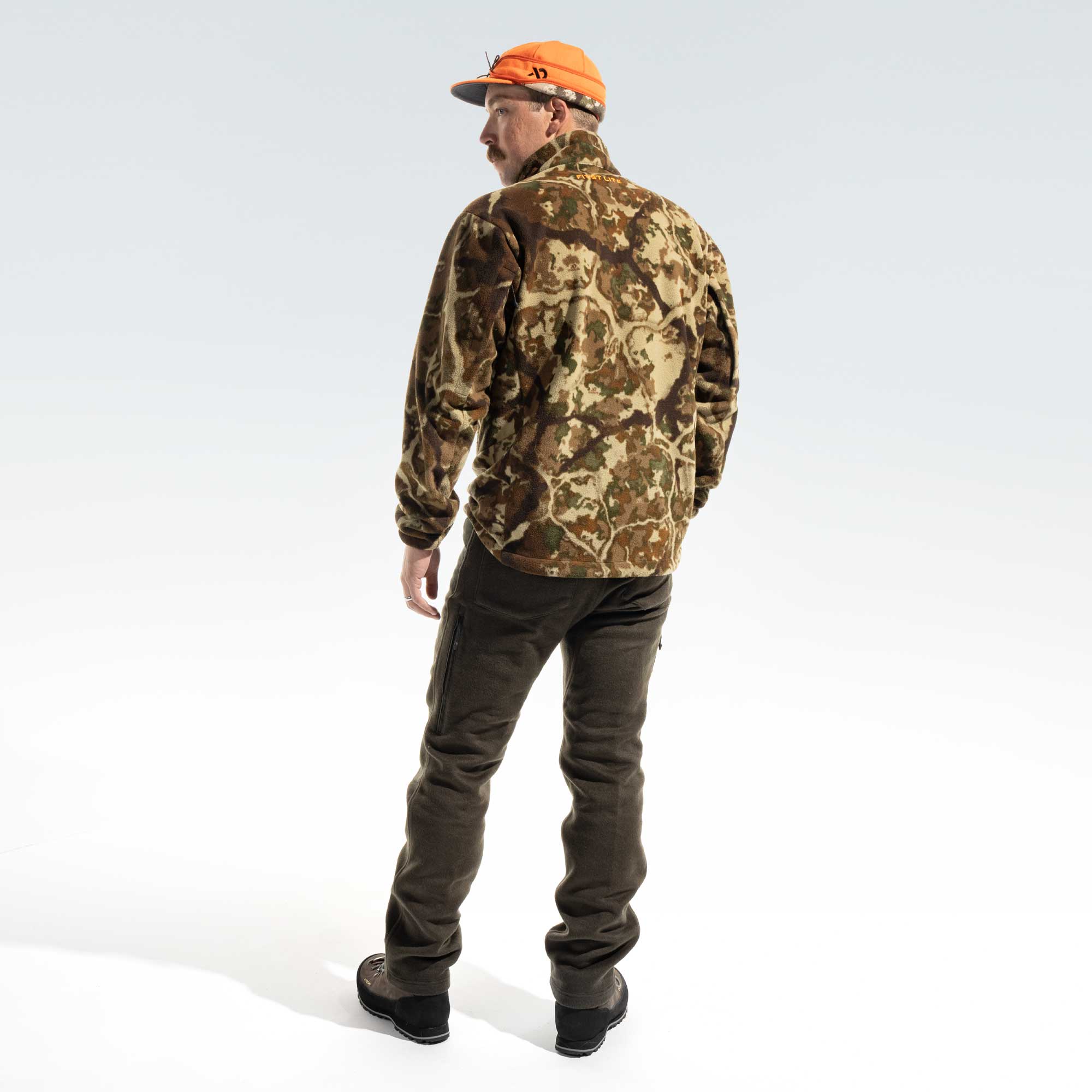 Behind shot of a man wearing an orange cap, camo jacket, dark moss pants and brown boots.