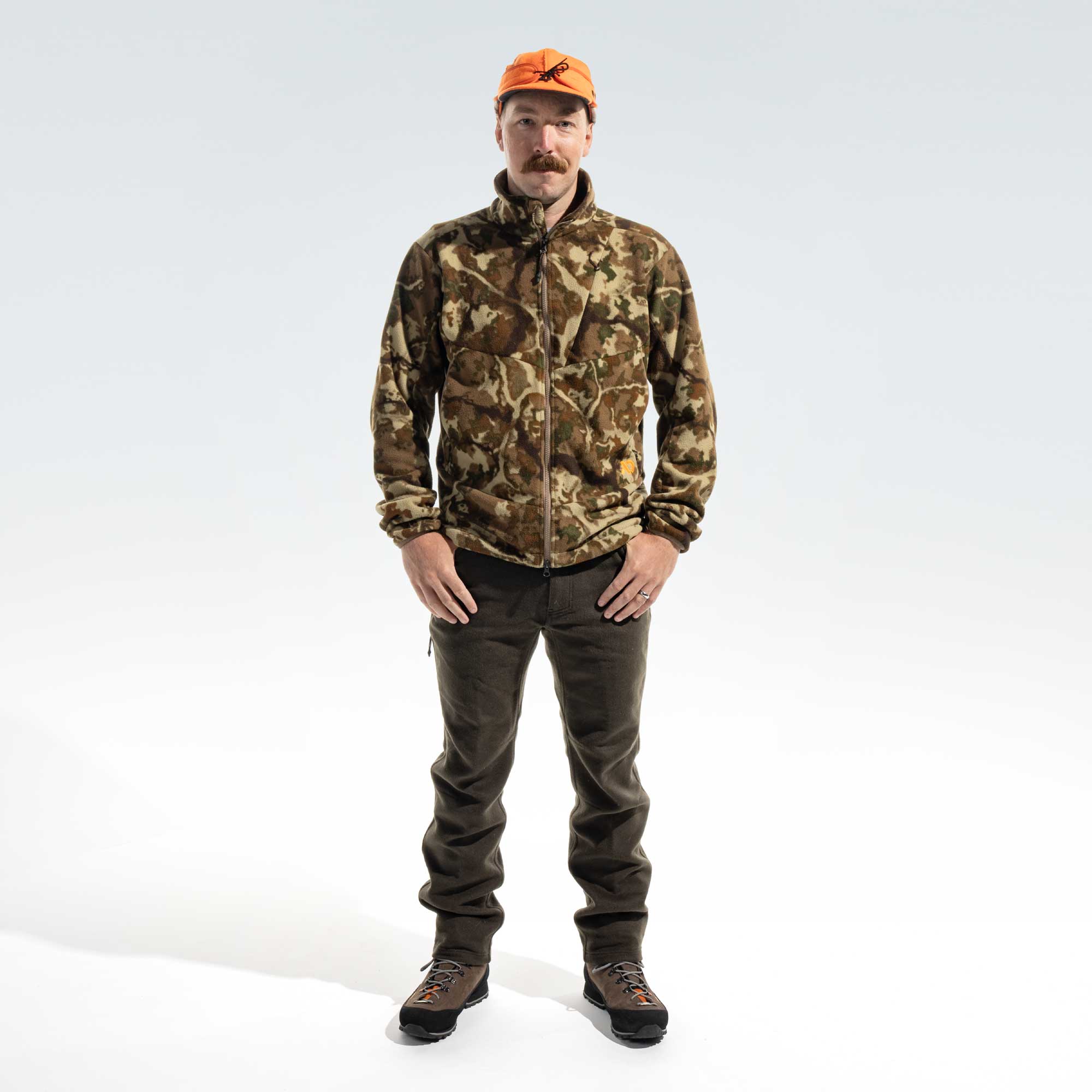 Man wearing an orange cap, camo jacket, dark moss pants and brown boots.