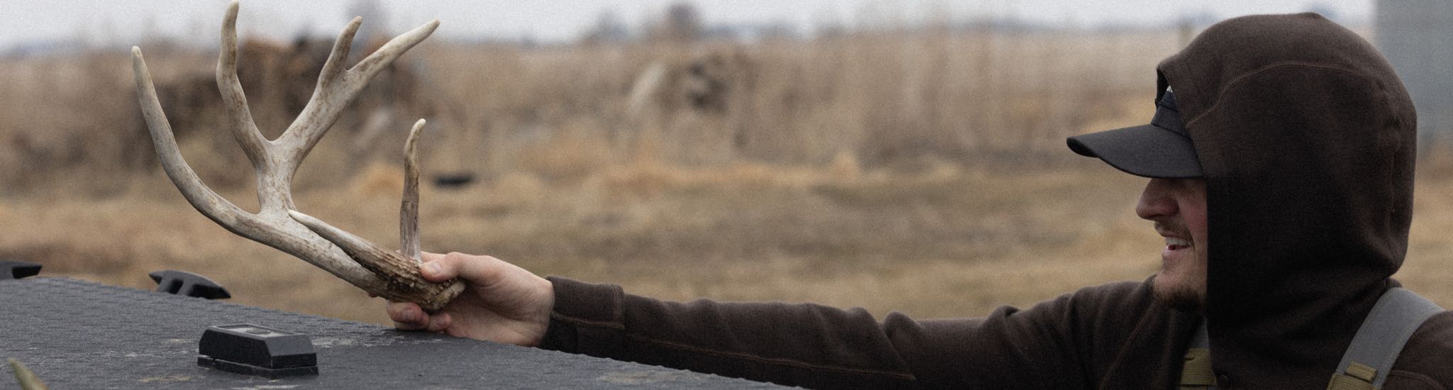 Smiling man in brown hoodie holds a large, tan, multi-pointed deer antler.
