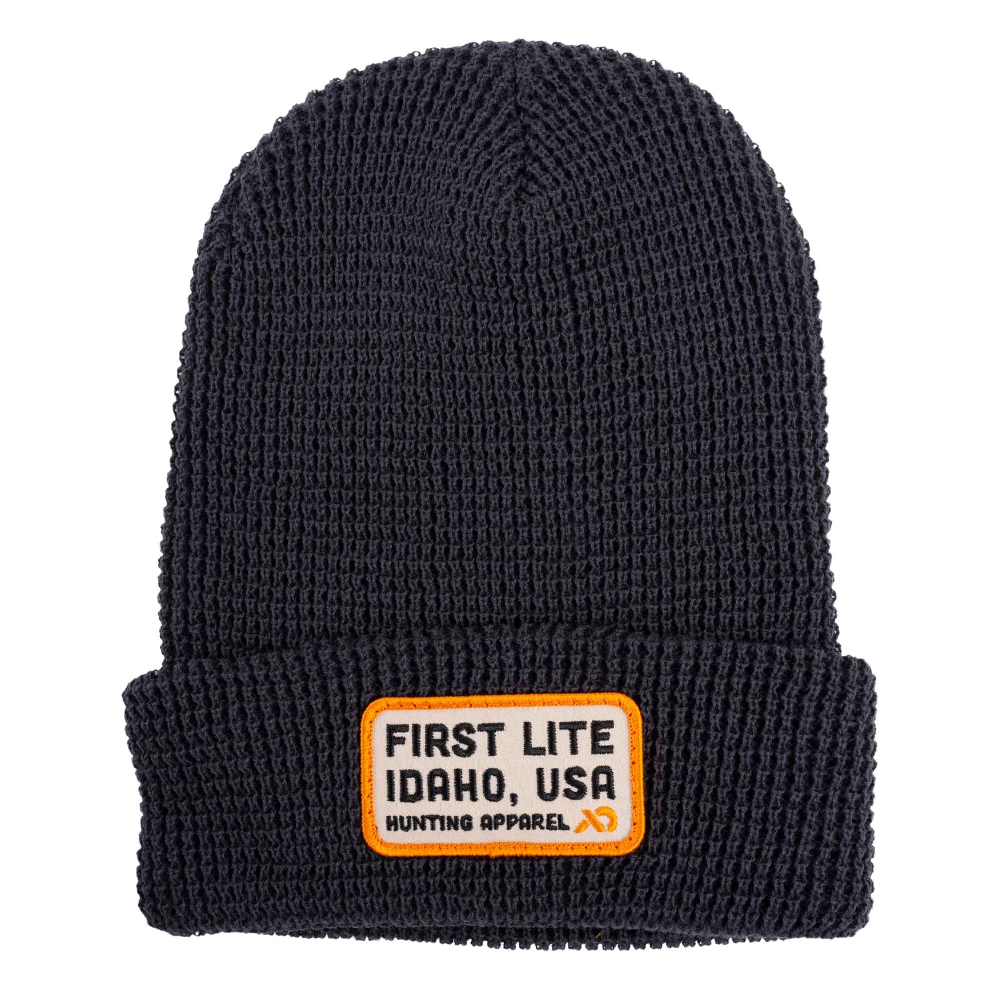 Dark grey ribbed knit beanie with a folded cuff and a beige square patch featuring the text "FIRST LITE IDAHO, USA Hunting Apparel"