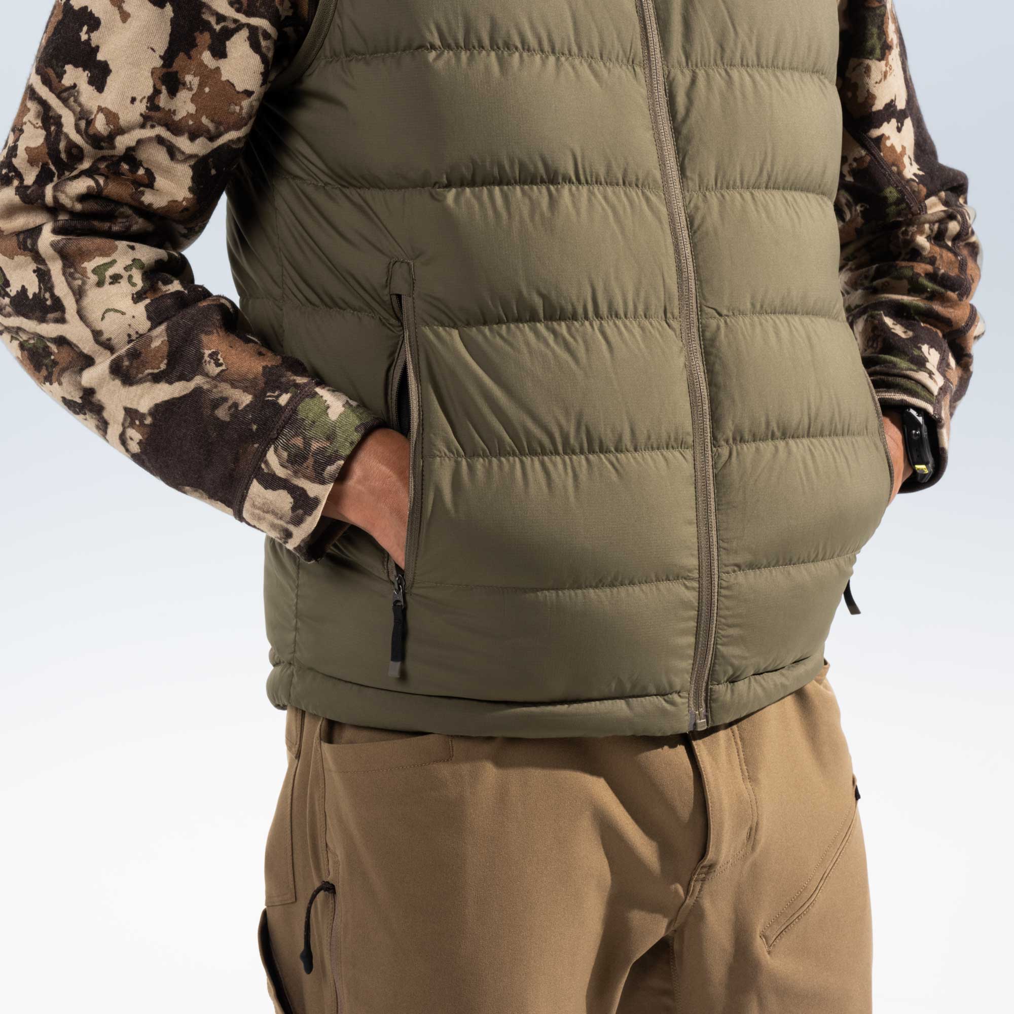 Close up of a man wearing a green puffer vest with his hands in his pockets. 