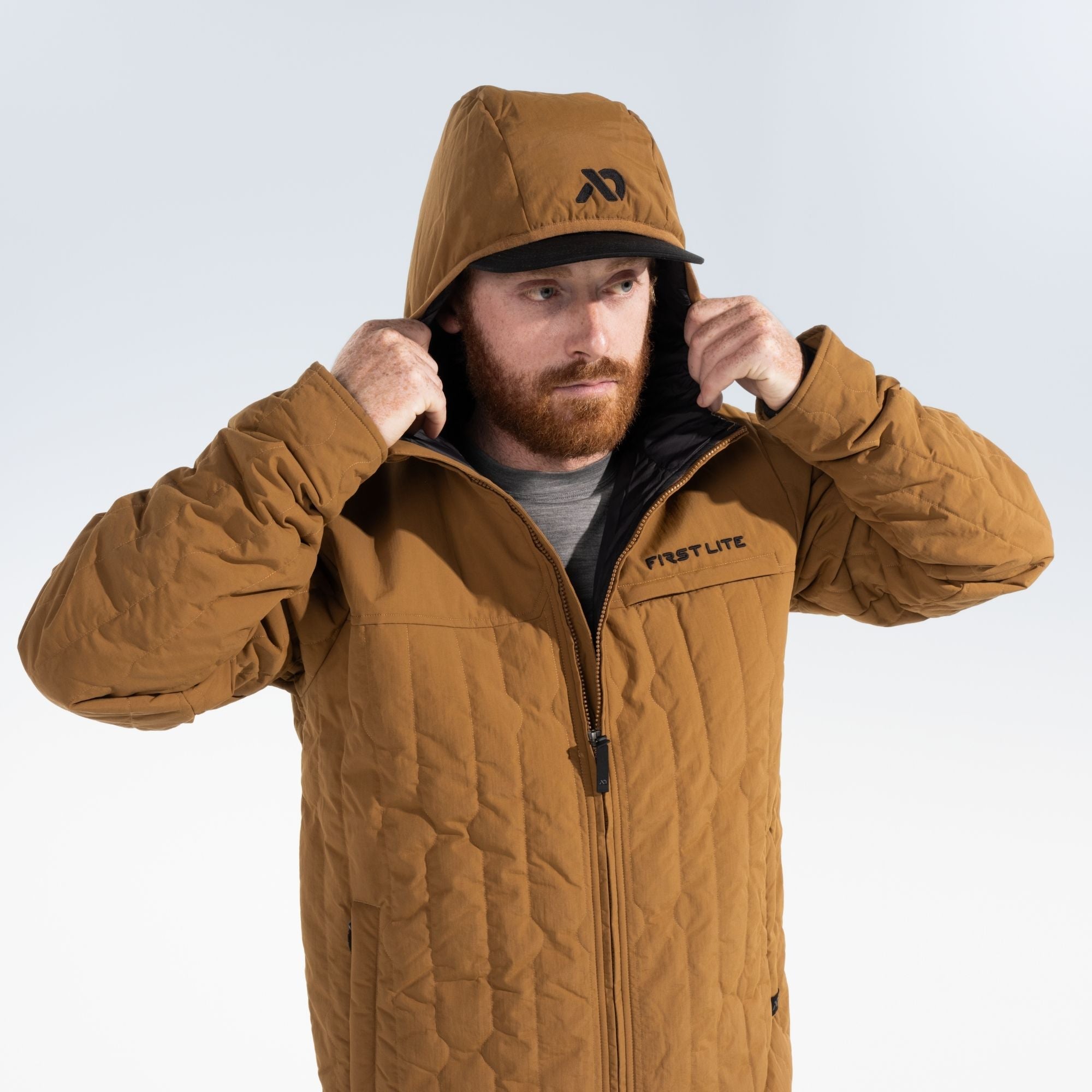Man wearing a rust outpost jacket that has black FIRST LITE branding on the left chest and black FIRST LITE logo on the jacket hood.