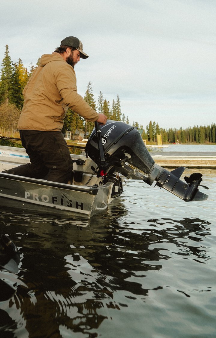 Man adjusting an outboard motor on a Pro Fish boat on a lake with trees in the background