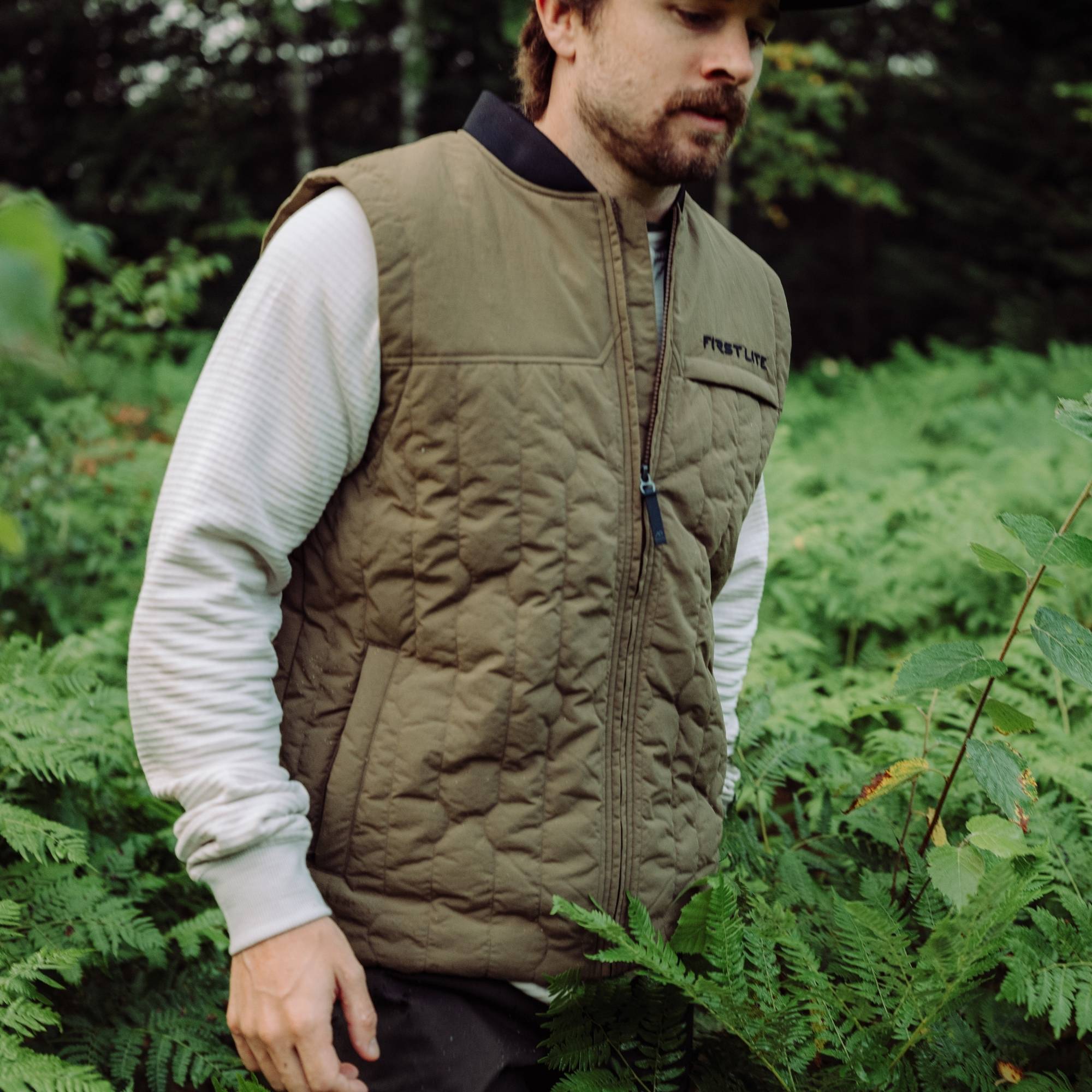 Man wearing an akern outpost vest over a light gray shirt in the forest.