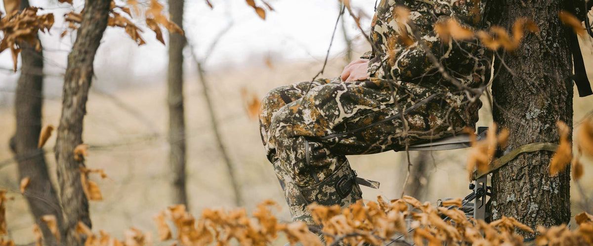 Close up of a hunter sitting in a tree stand wearing whitetail camo, boots, and insulated outerwear.