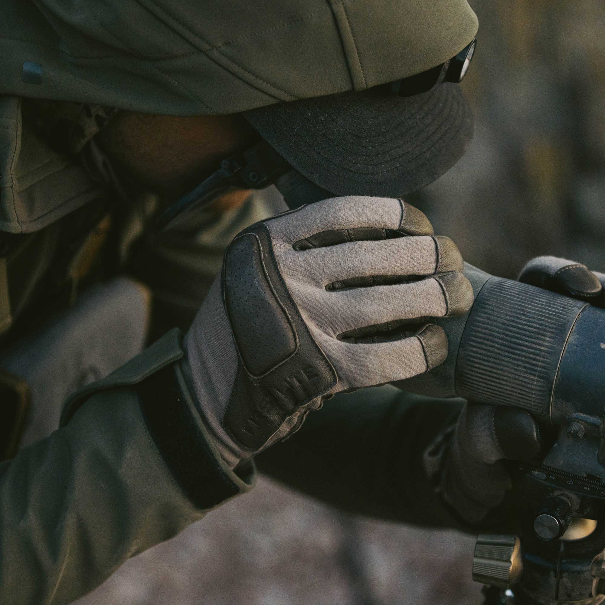 A close-up shot of a person light tan and leather gloves while looking through a spotting scope. 